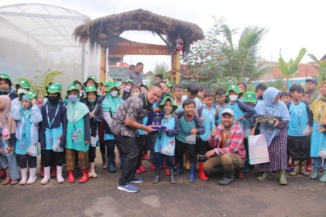 Students in green hats and boots gathered with teachers at a school garden