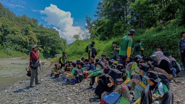 Students sitting on a riverbank during an outdoor learning activity